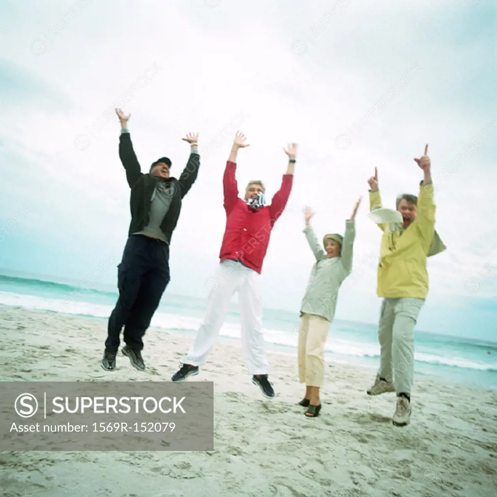 Mature group on beach, jumping in air, looking into camera