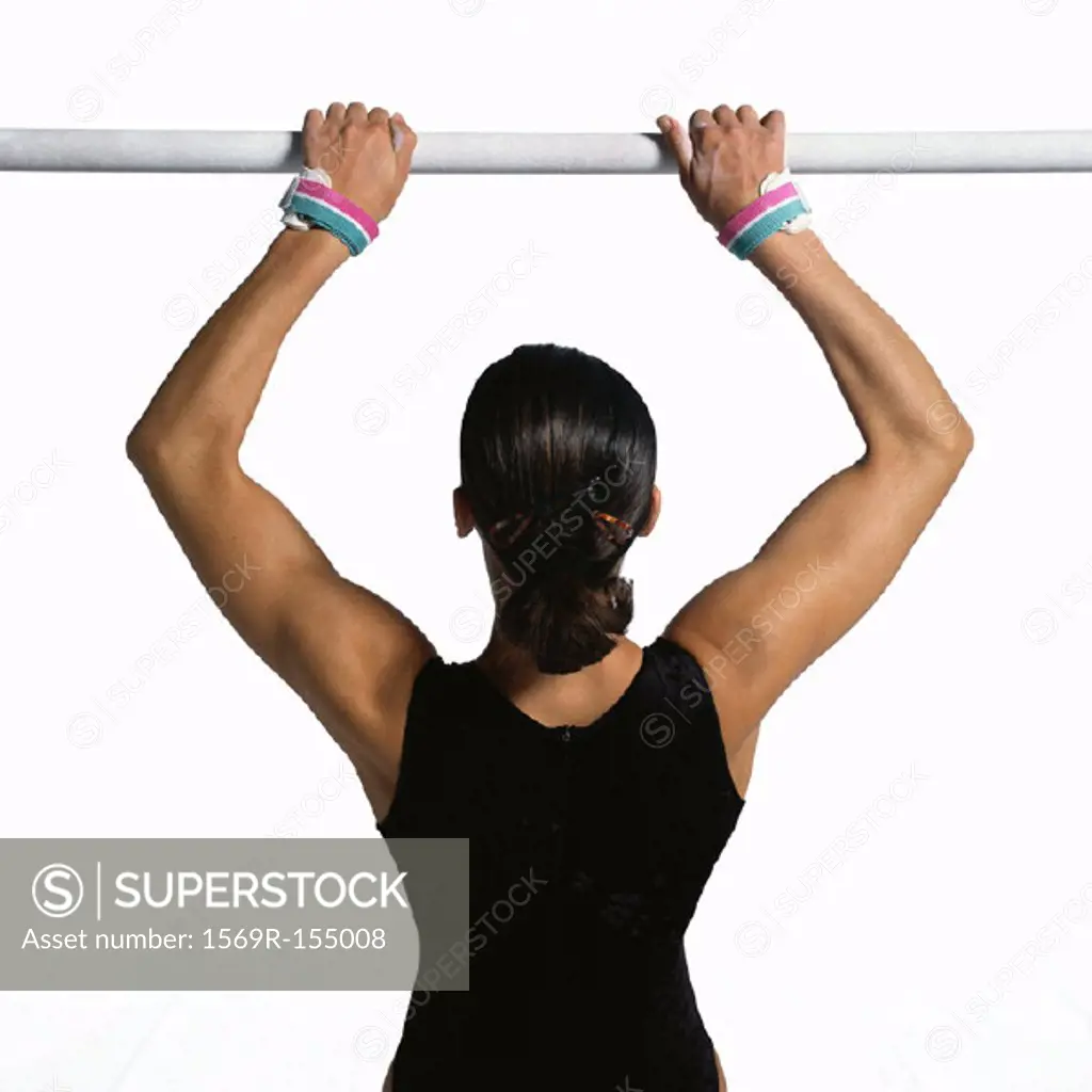 Female gymnast pulling herself up on horizontal bar, upper section, rear view