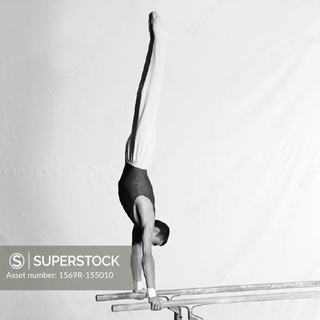 Young male gymnast doing handstand on parallel bars, side view
