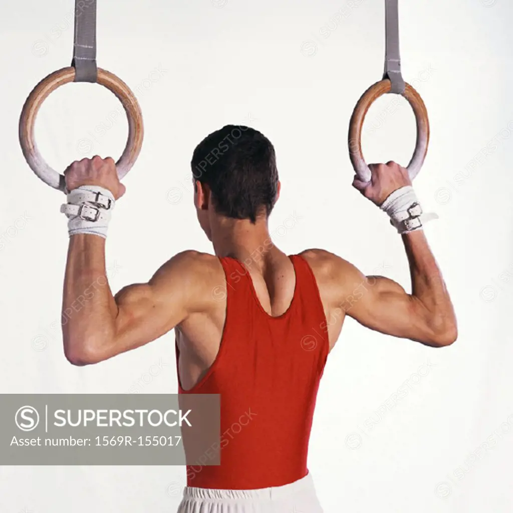Male gymnast pulling himself up on rings, upper section, rear view
