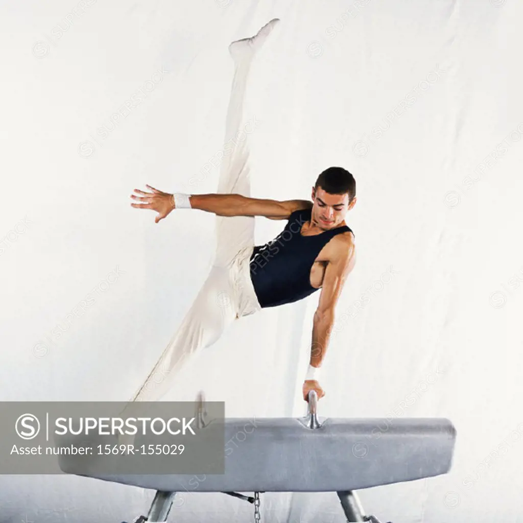 Young male gymnast performing scissors routine on pommel horse