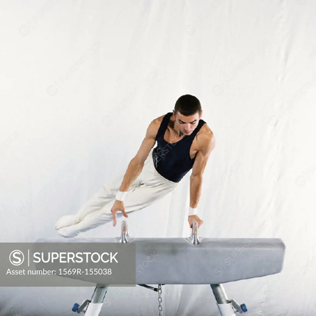 Young male gymnast performing routine on pommel horse