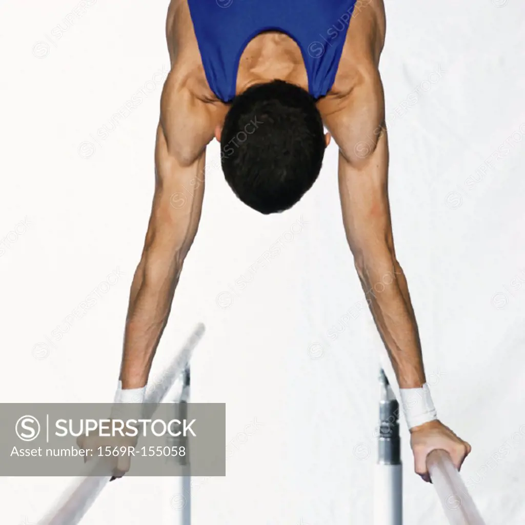 Male gymnast performing handstand on parallel bars, upper section, rear view