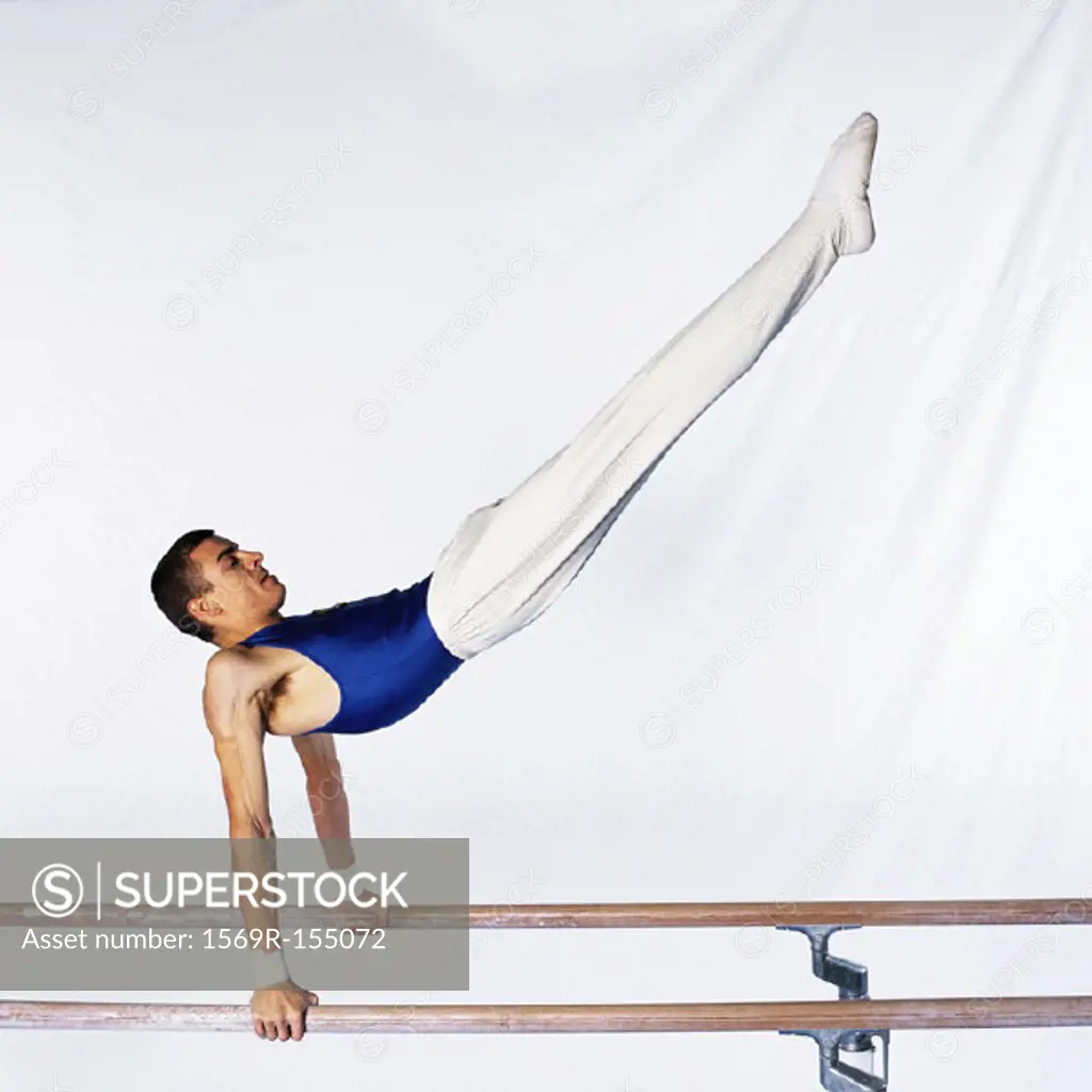 Young male gymnast performing routine on parallel bars, side view