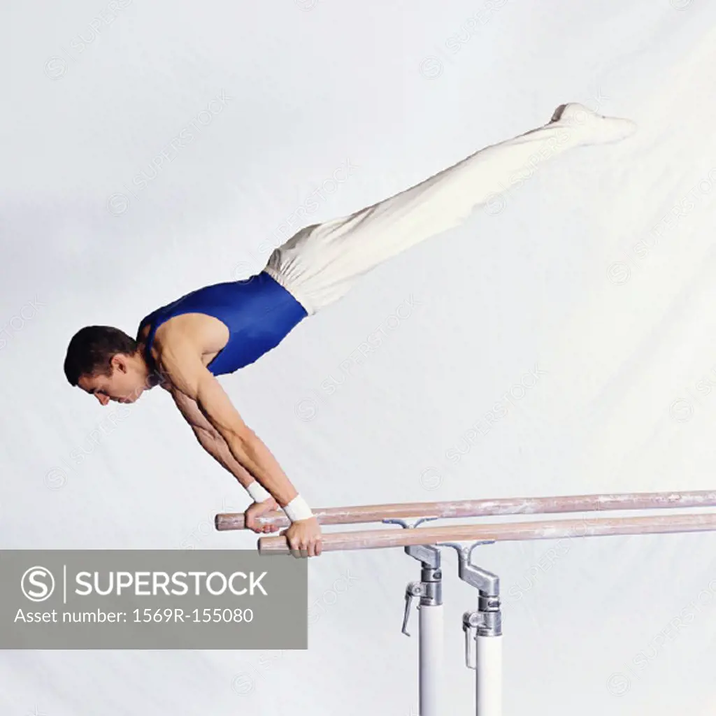 Young male gymnast performing routine on parallel bars