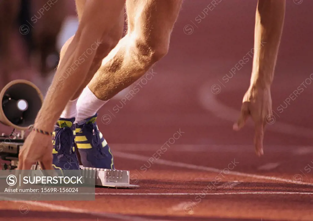 Male runner leaving starting block, low section, close-up