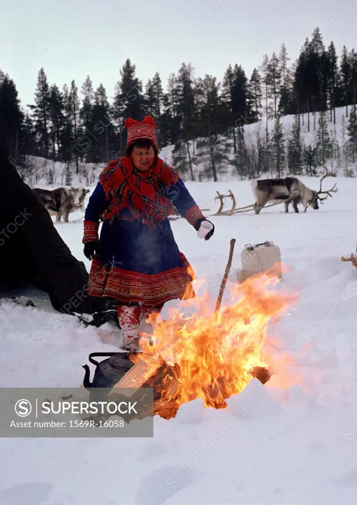 Finland, Saami woman standing next to fire, sled reindeer in background