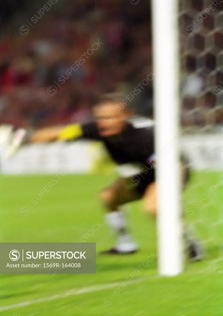 Goal keeper defending goal in soccer match, blurred