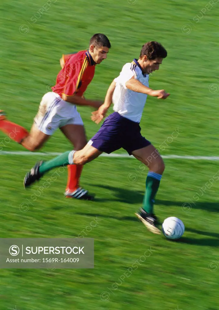 Soccer player running with ball, opponent chasing him, full length, blurred