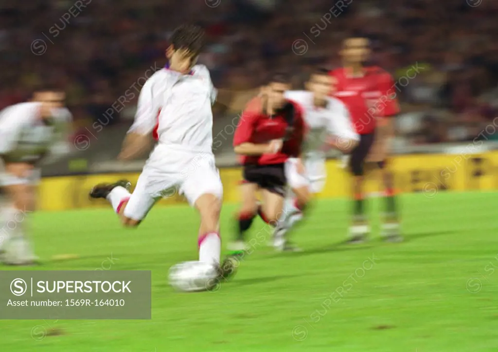 Soccer player about to kick ball, four players in background, blurred