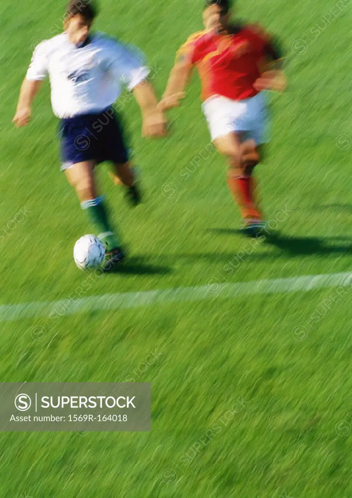 Soccer player running with ball, opponent chasing him, blurred
