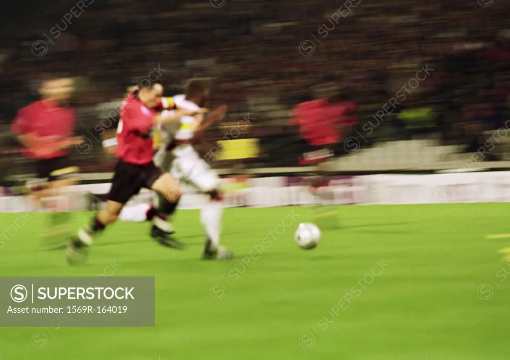 Two soccer players running for ball, blurred