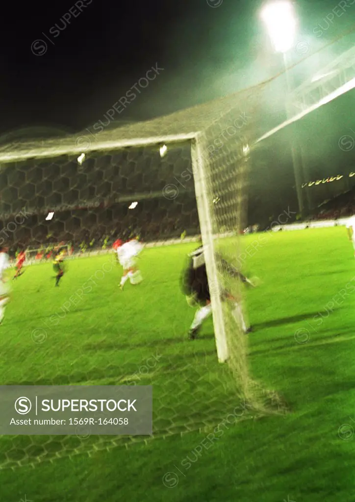 Soccer players during a game, seen from behind the goal, blurred