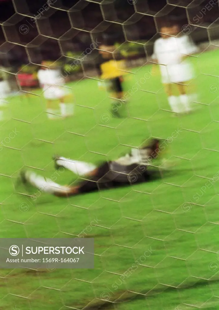 Goal keeper on ground in front of goal, blurred