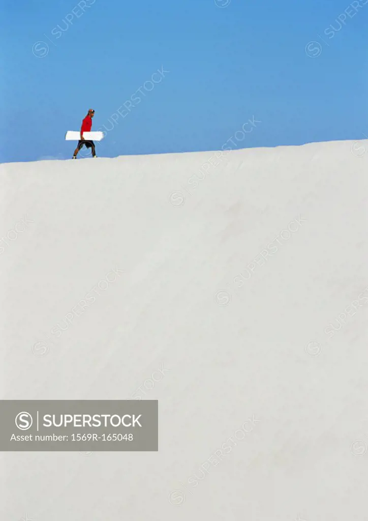 Man walking across dune with snowboard
