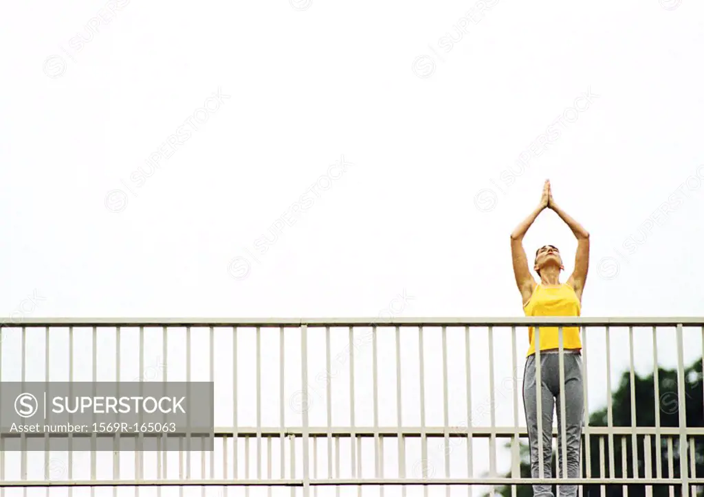 Woman standing on bridge, hands over head, low angle view
