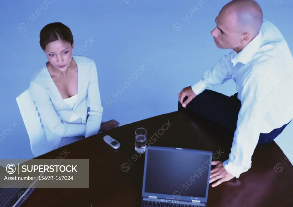 Businesswoman in chair, man sitting on desk, elevated view