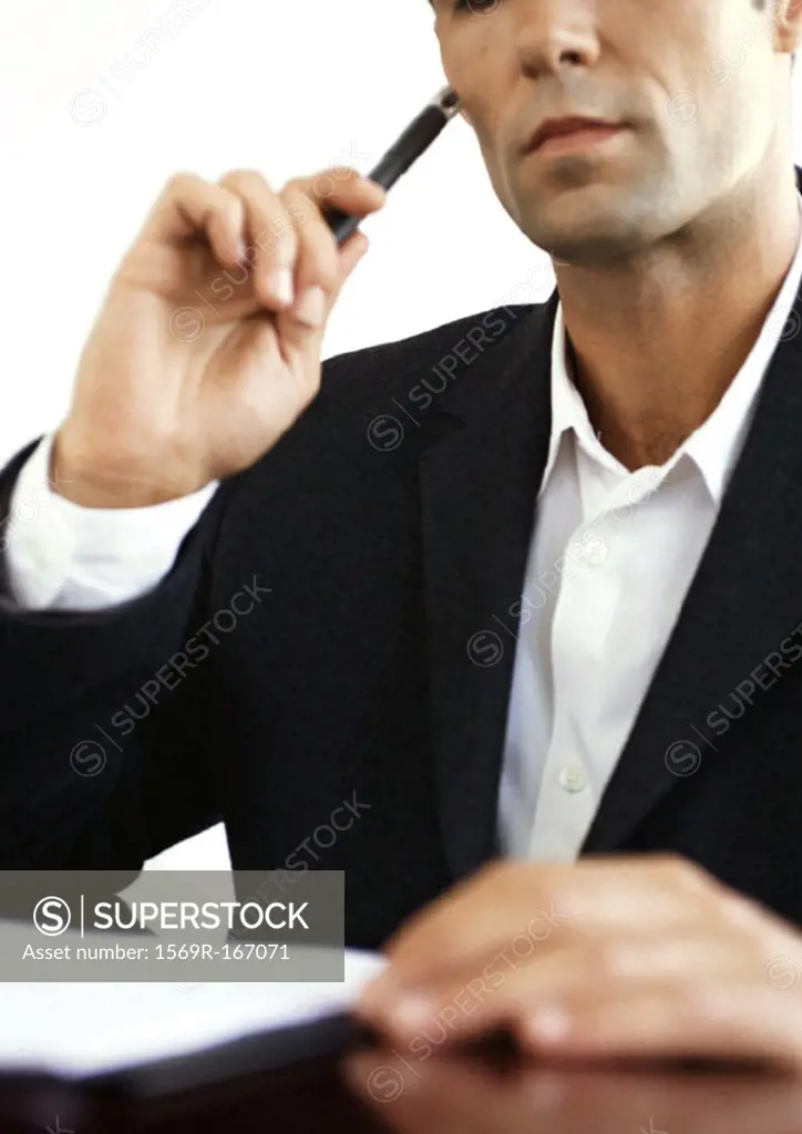 Businessman at desk, holding pencil, close-up