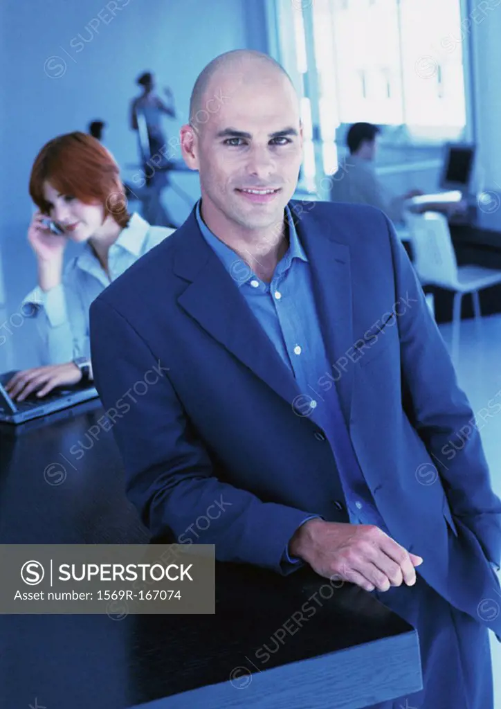 Businesspeople in office, man smiling at camera, portrait