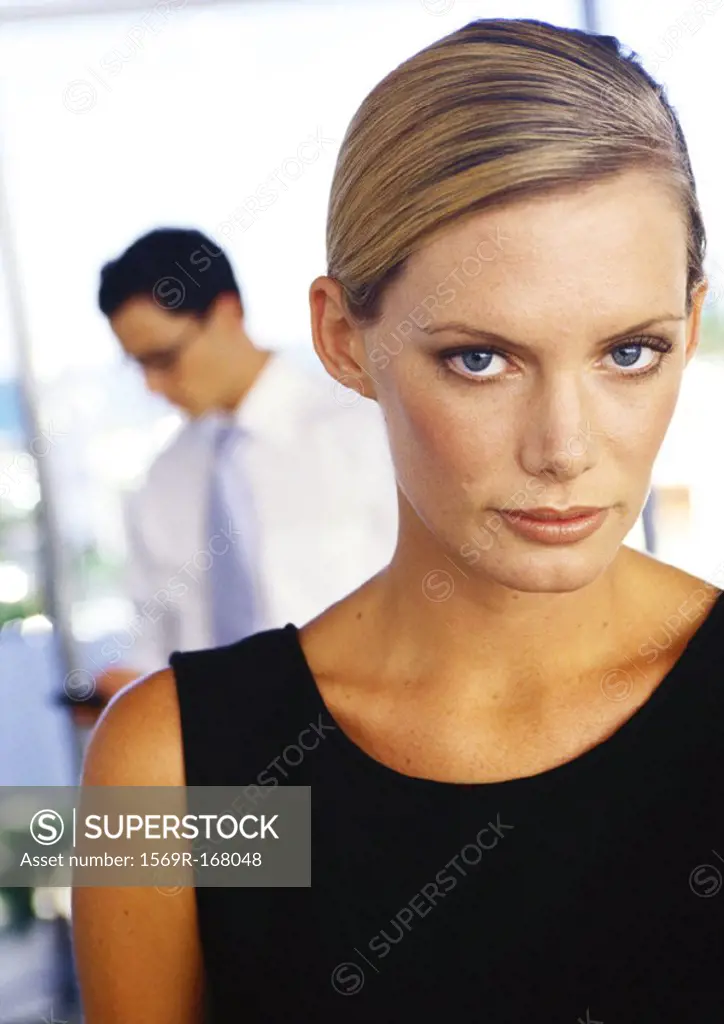 Businesswoman looking into camera, businessman in background