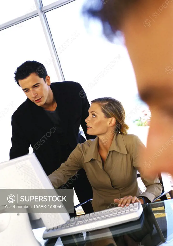 Businessman and woman using computer, second man´s face blurred in foreground