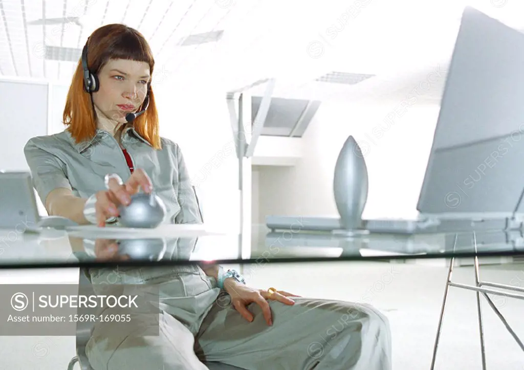 Woman wearing headset, sitting at desk, three quarter length