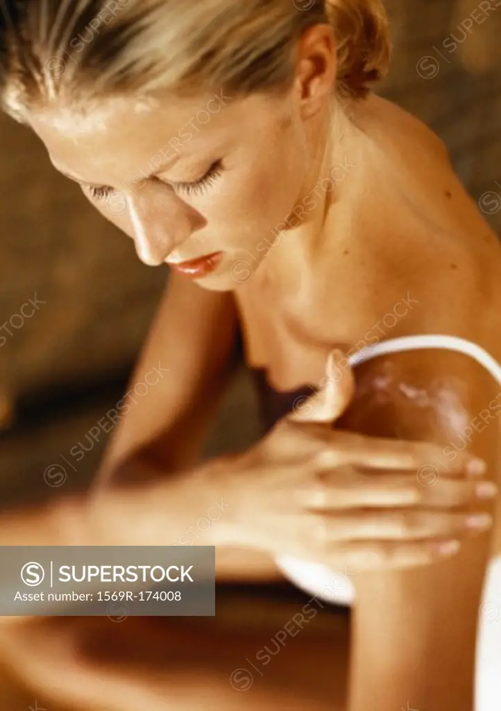 Woman putting lotion on shoulder, high angle view