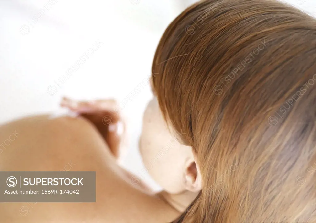 Woman applying cream to elbow, rear view, blurred