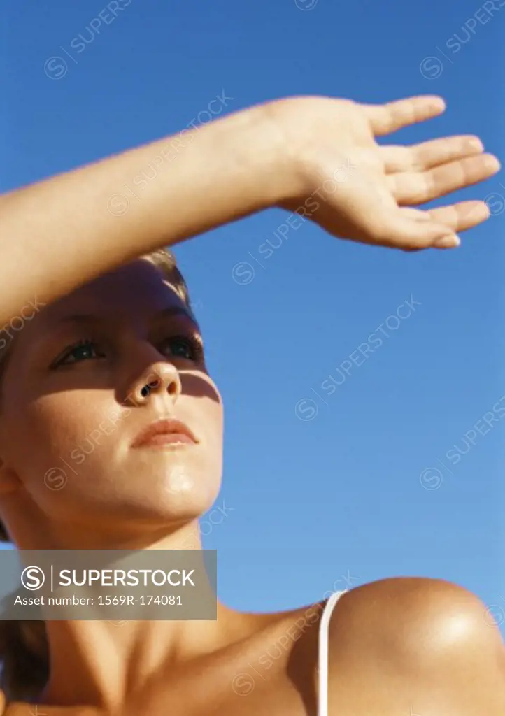 Woman protecting eyes from sun with hand, close-up