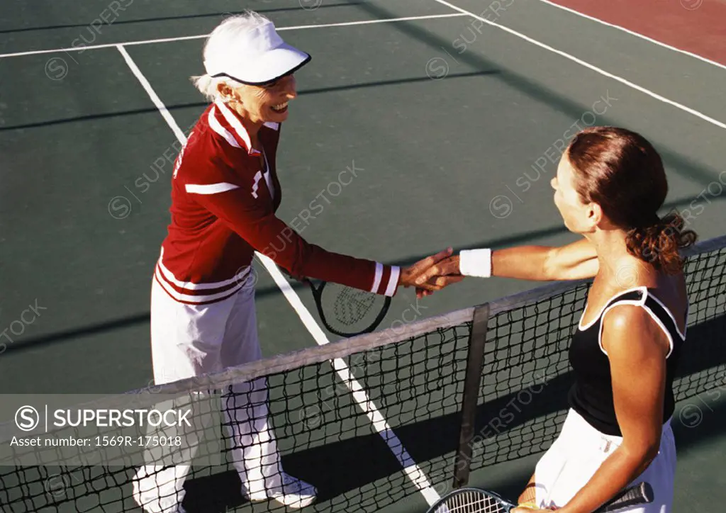 Two mature women shaking hands on tennis court