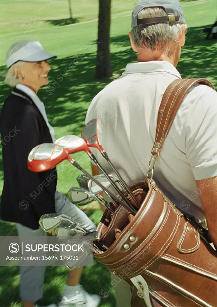 Two mature golfers, one carrying clubs, rear view