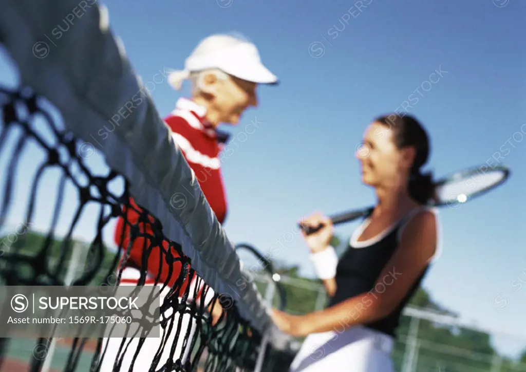 Two mature women talking on tennis court, blurred