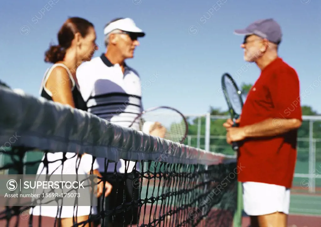 Three mature tennis players on court, side view