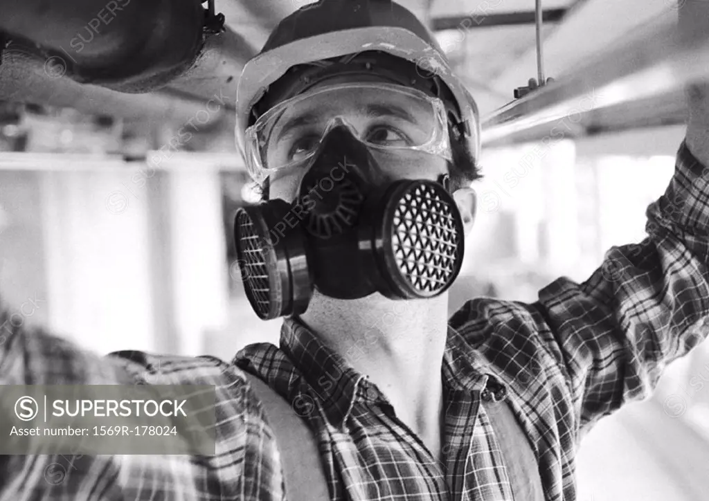 Man wearing hard hat, dust mask and protective glasses, close-up, b&w