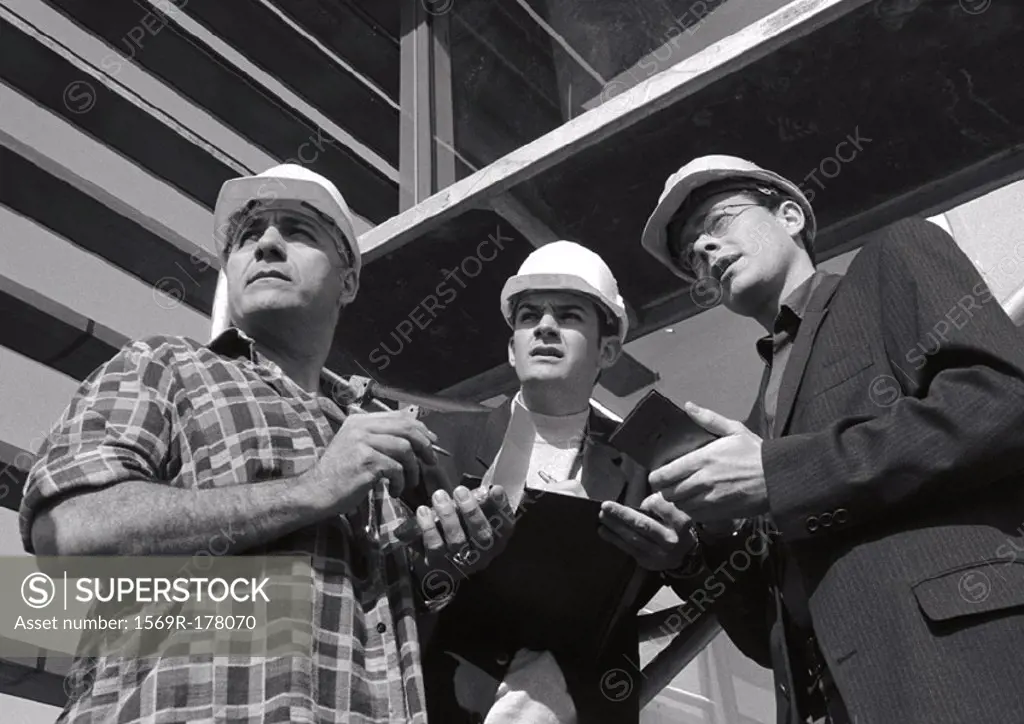 Three men wearing hard hats, holding notepads, b&w