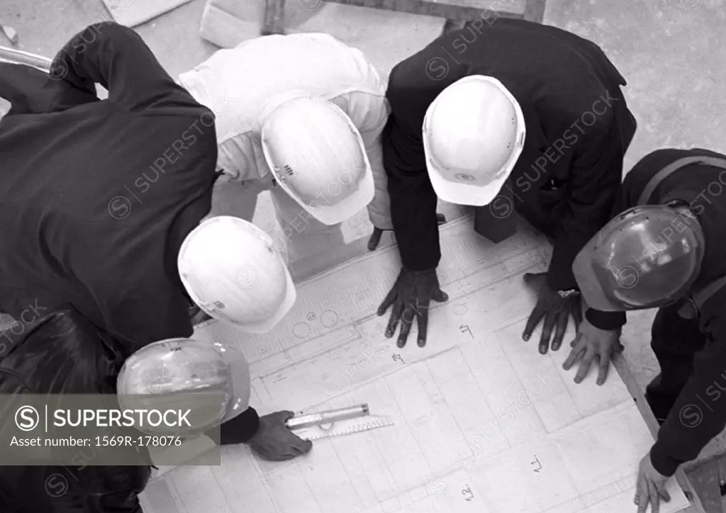 Five people with hard hats, examining blueprints, elevated view, b&w