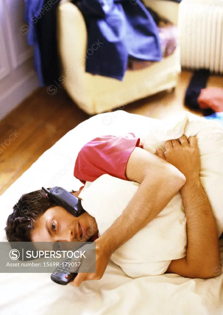Man lying on bed with phone and remote control