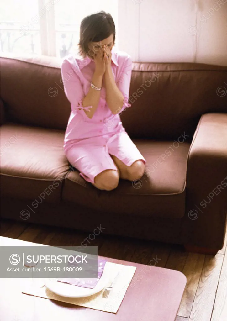 Woman kneeling on sofa, hands over face