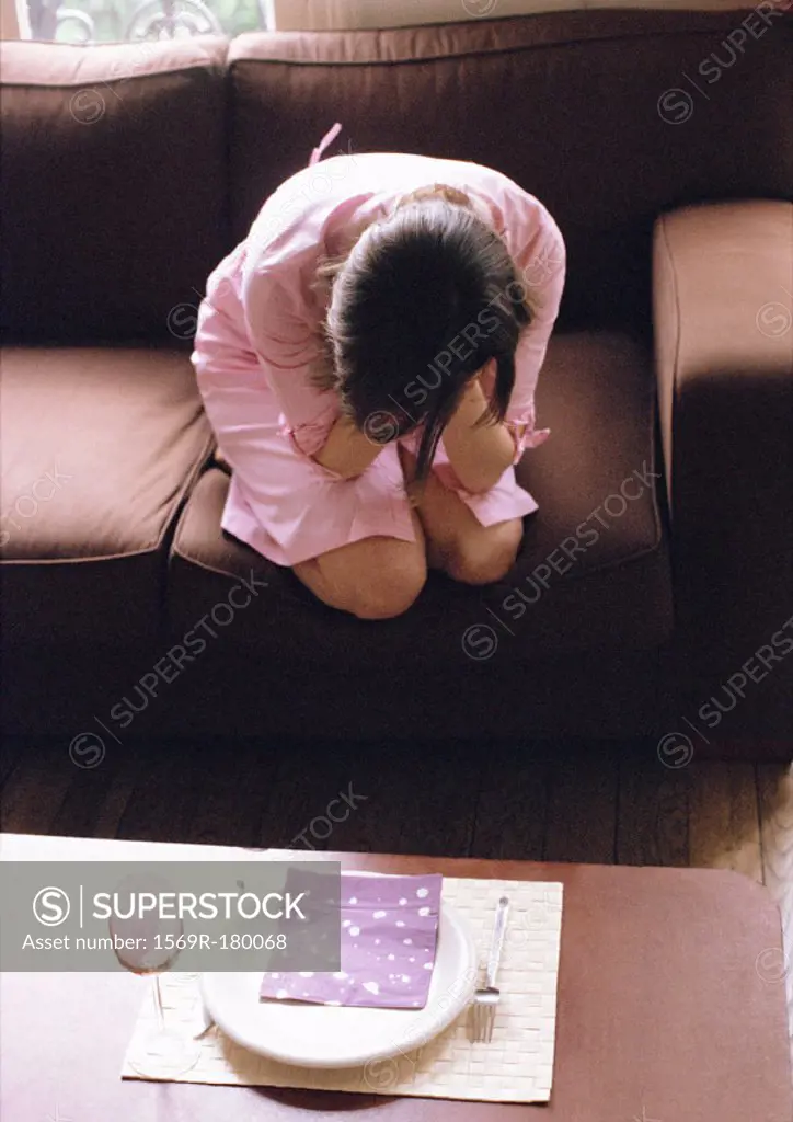 Woman kneeling on sofa, head in hands