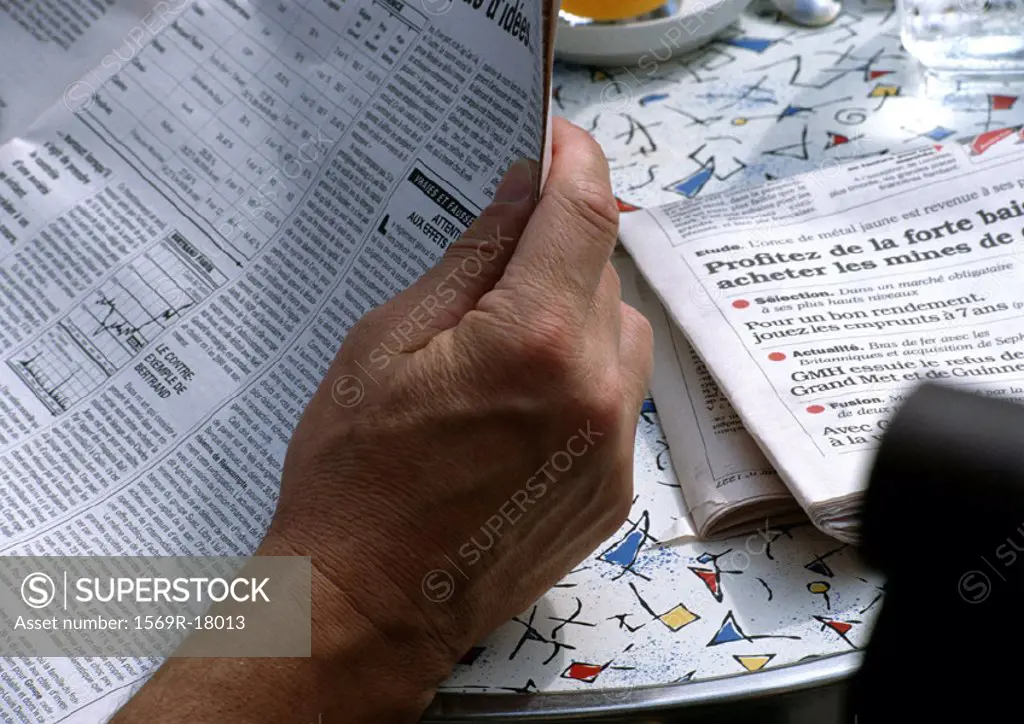 Man reading newspaper at table, close up of paper