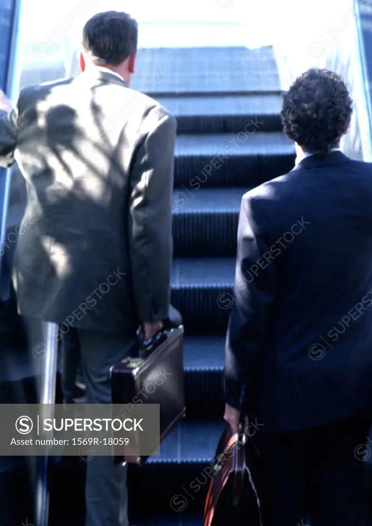 Businessmen riding escalator, rear view