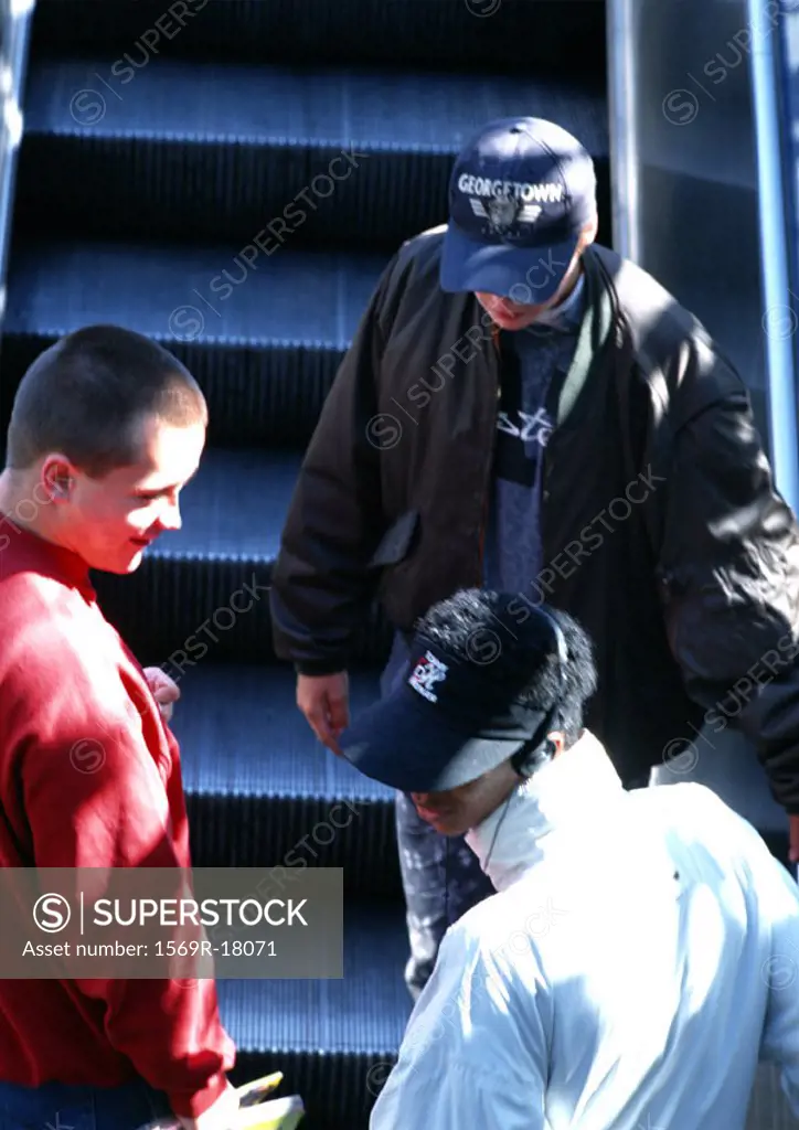 Young men riding escalator, rear view