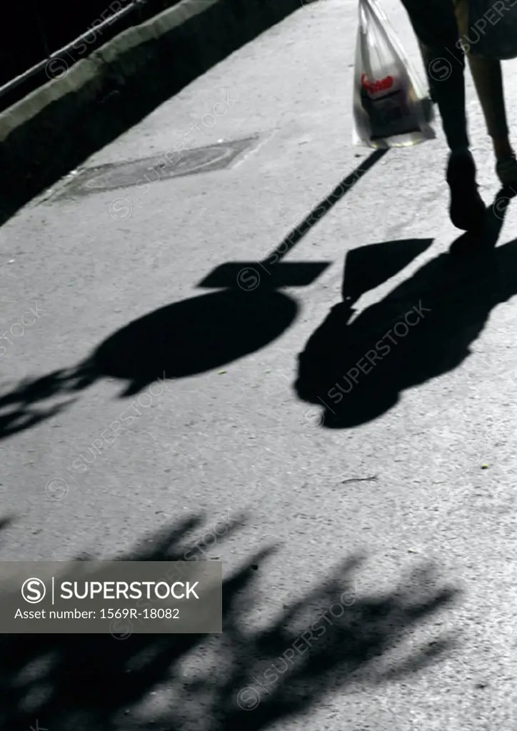 Person walking on street with bag, shadows