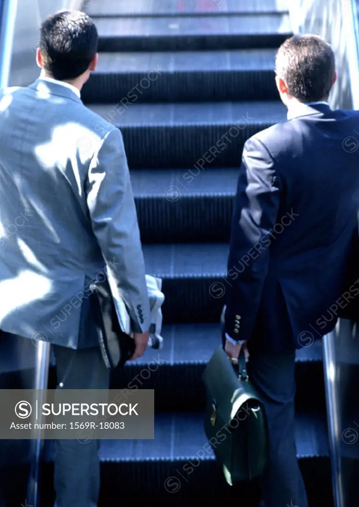 Businessmen riding escalator, rear view