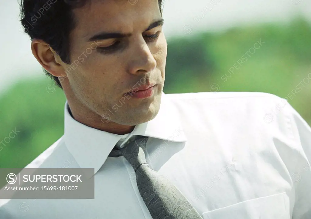 Businessman outdoors, looking down, close-up