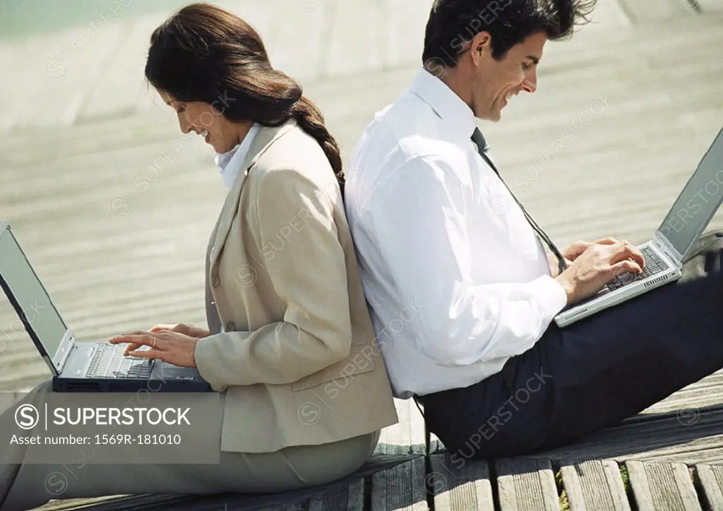 Businessman and woman back to back on ground with laptop computers on laps