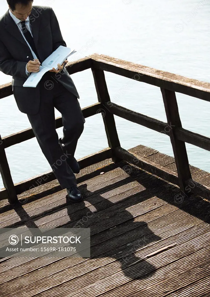 Businessman leaning on railing above water