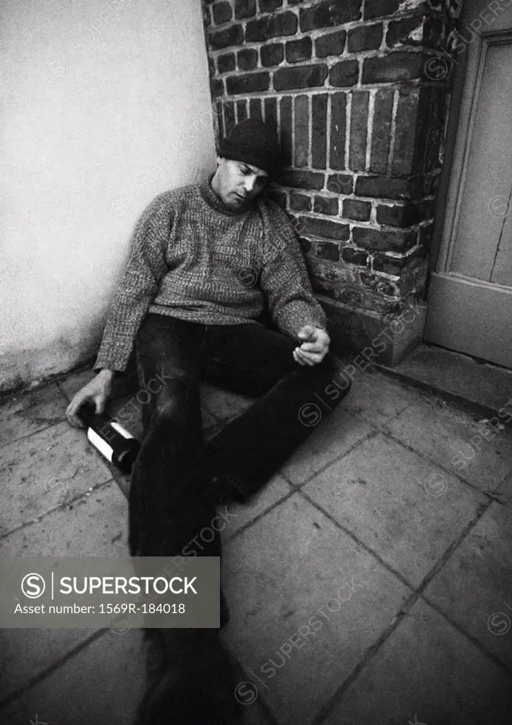 Man sitting on ground with bottle in hand and eyes closed