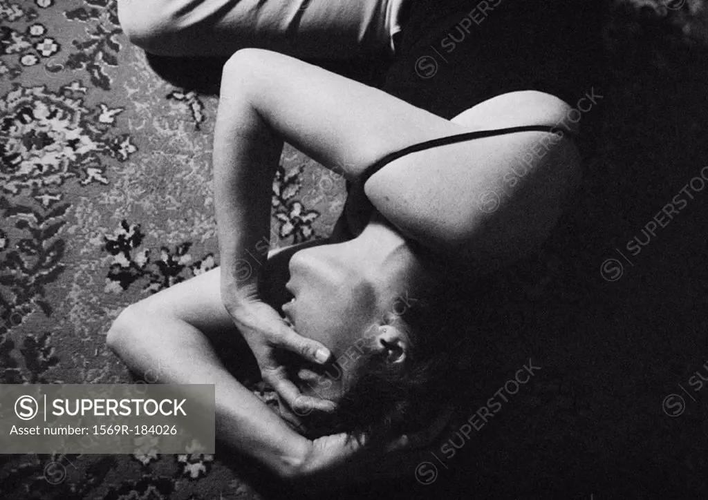 Woman lying curled up on floor, holding head, b&w