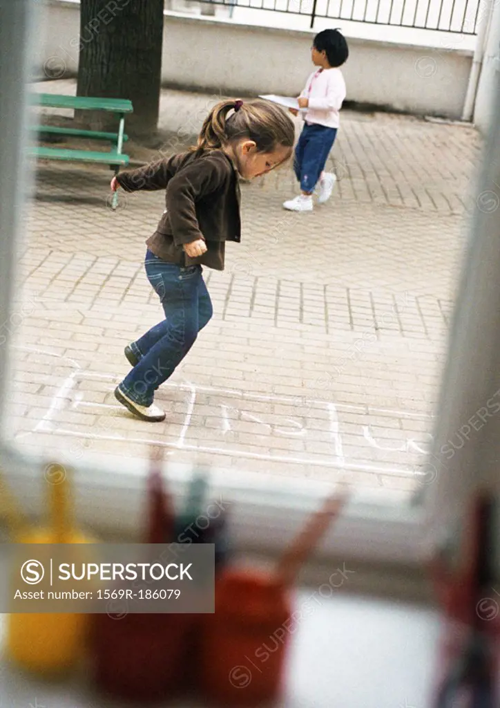 Children outdoors, one playing hopscotch, side view
